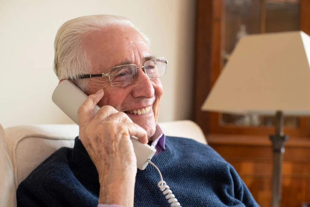 Älterer Herr telefoniert lächelnd mit Festnetz-Telefon.