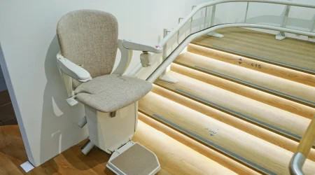 Ein Treppenlift mit gepolstertem Sitz und Armlehnen ist an einer geschwungenen Treppe montiert.