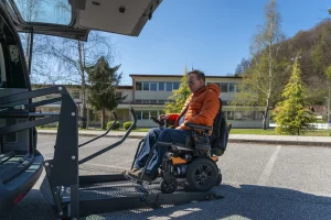 Mann mittleren Alters fährt per Rampe mit seinem elektrischen Rollstuhl in den Kofferraum eines Autos