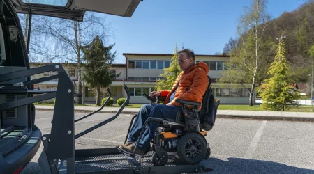 Mann mittleren Alters fährt per Rampe mit seinem elektrischen Rollstuhl in den Kofferraum eines Autos
