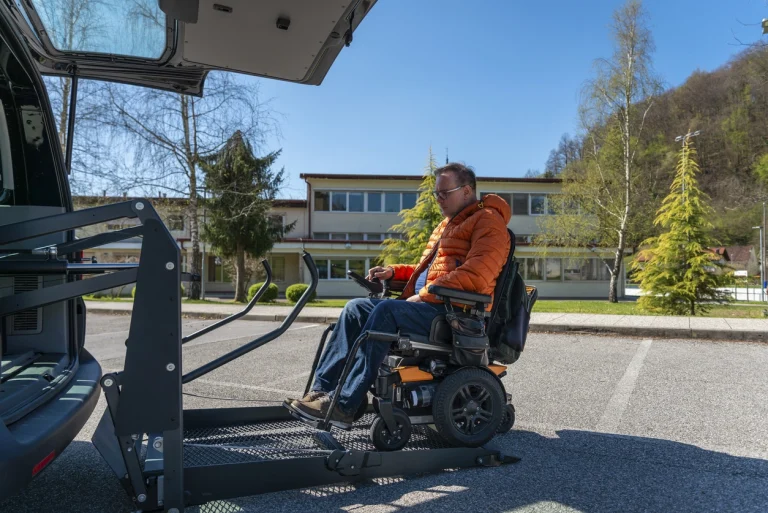 Mann mittleren Alters fährt per Rampe mit seinem elektrischen Rollstuhl in den Kofferraum eines Autos