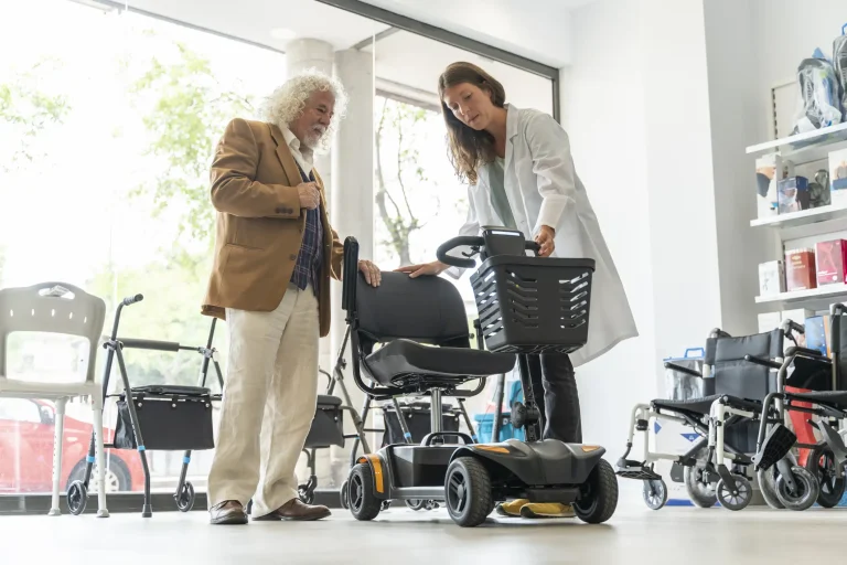 Älterer Mann in einem Sanitätshaus lässt sich von einer Mitarbeiterin ein Elektromobil zeigen. Im Hintergrund sind Rollatoren und Rollstühle ausgestellt.