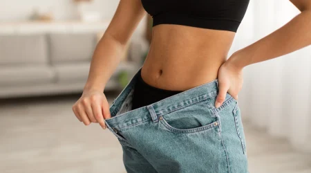 Eine Frau zieht den Bund ihrer Jeans von ihrem Bauch weg, um zu signalisieren, dass sie abgenommen hat.