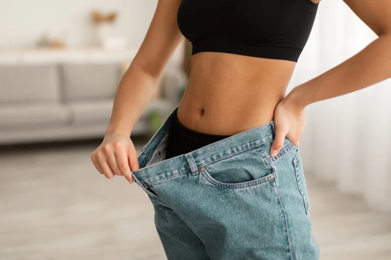 Eine Frau zieht den Bund ihrer Jeans von ihrem Bauch weg, um zu signalisieren, dass sie abgenommen hat.