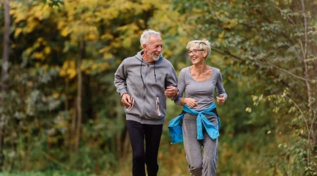 Ein älterer Mann und eine ältere Frau joggen gemeinsam durch den Wald, um sich fit zu halten.