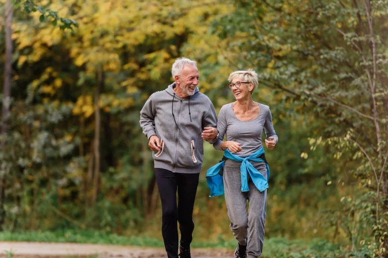 Ein älterer Mann und eine ältere Frau joggen gemeinsam durch den Wald, um sich fit zu halten.