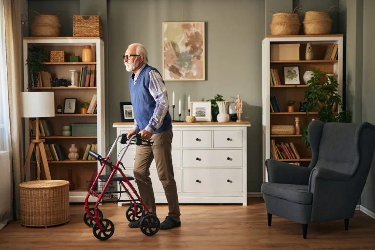 Ein älterer Mann geht mithilfe seines Rollators durch sein Wohnzimmer.