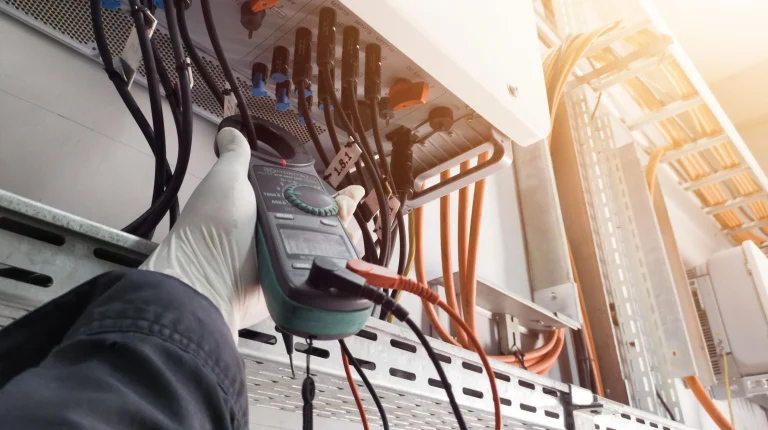 Solarteur misst mit einem Multimeter die elektrischen Anschlüsse einer Photovoltaikanlage zur Prüfung nach DIN VDE 4105.