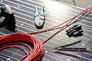 PV-Komponenten auf einem Solarmodul, darunter rote Solarkabel, MC4-Stecker, Crimpwerkzeug und Anschlussleitungen für die Installation einer Photovoltaikanlage.