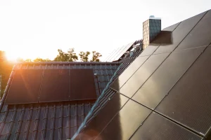 Dach eines Wohnhauses mit integrierten Photovoltaikmodulen bei tief stehender Sonne und sichtbarem Schornstein.