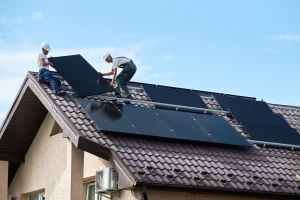 Zwei Solarteure montieren Photovoltaikmodule auf einem geneigten Ziegeldach eines Einfamilienhauses unter freiem Himmel.