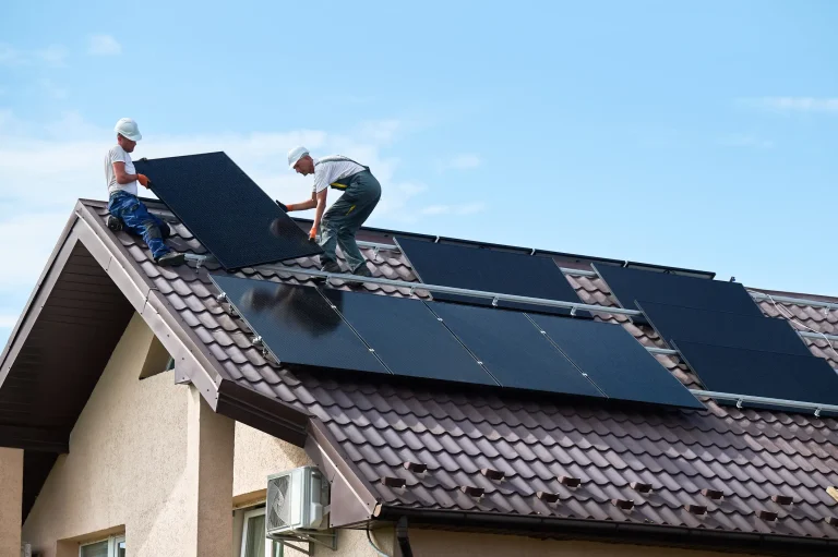 Zwei Solarteure montieren Photovoltaikmodule auf einem geneigten Ziegeldach eines Einfamilienhauses unter freiem Himmel.