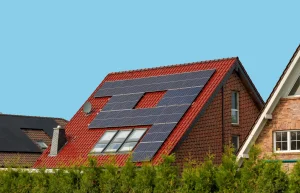 Photovoltaikanlage auf einem roten Ziegeldach. Mehrere Solarmodule sind um Dachfenster herum montiert, vor blauem Himmel.