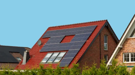 Photovoltaikanlage auf einem roten Ziegeldach. Mehrere Solarmodule sind um Dachfenster herum montiert, vor blauem Himmel.