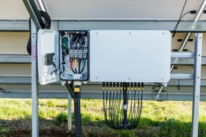 Geöffneter Wechselrichter einer Photovoltaikanlage unter Solarmodulen mit sichtbarer Verkabelung und Anschlussklemmen.
