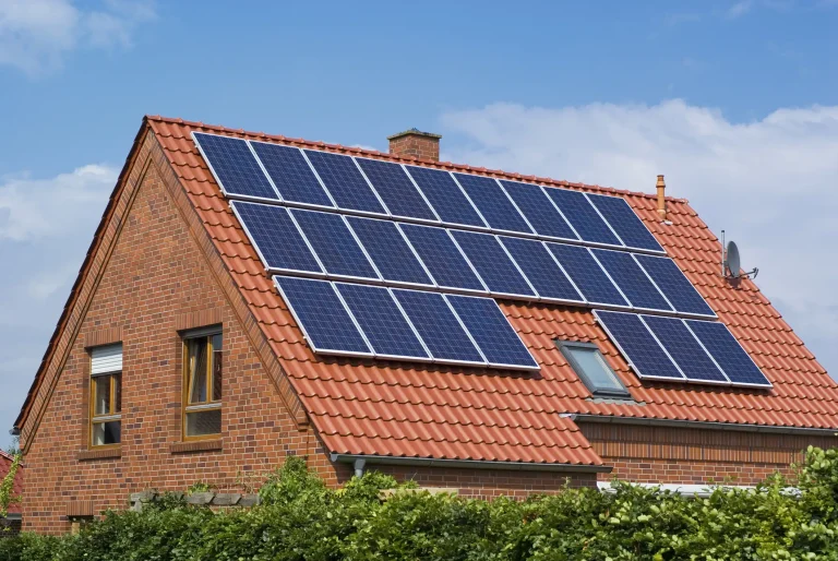 Eine großflächige Photovoltaikanlage mit 18 Solarmodulen, die auf dem roten Ziegeldach eines modernen Backsteinhauses montiert ist, unter blauem Himmel mit leichten Wolken.