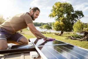 Junger Mann reinigt Solarpanels auf dem Dach seines Wohnmobils