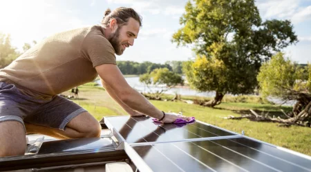 Junger Mann reinigt Solarpanels auf dem Dach seines Wohnmobils