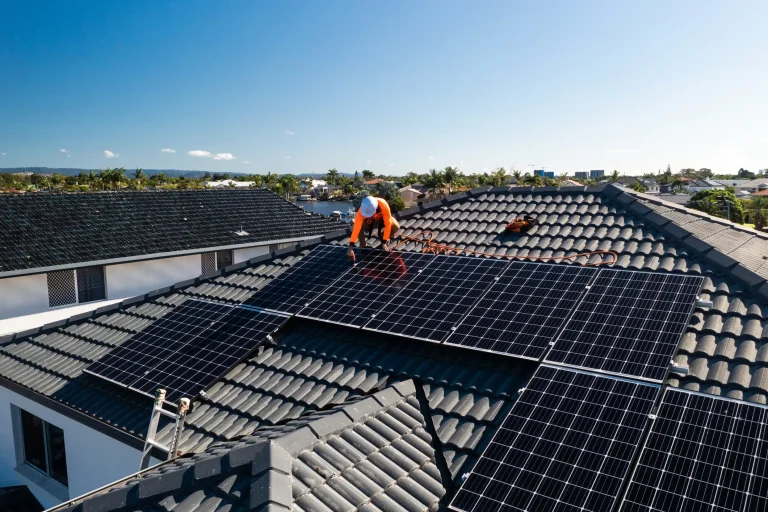 Ein Solarteur mit Sicherheitsausrüstung montiert Photovoltaik-Module auf einem anthrazitfarbenen Ziegeldach. Die fachgerechte Verankerung der Montageschienen im Dachstuhl ist entscheidend für die Statik bei PV-Anlagen unter Wind- und Schneelast.