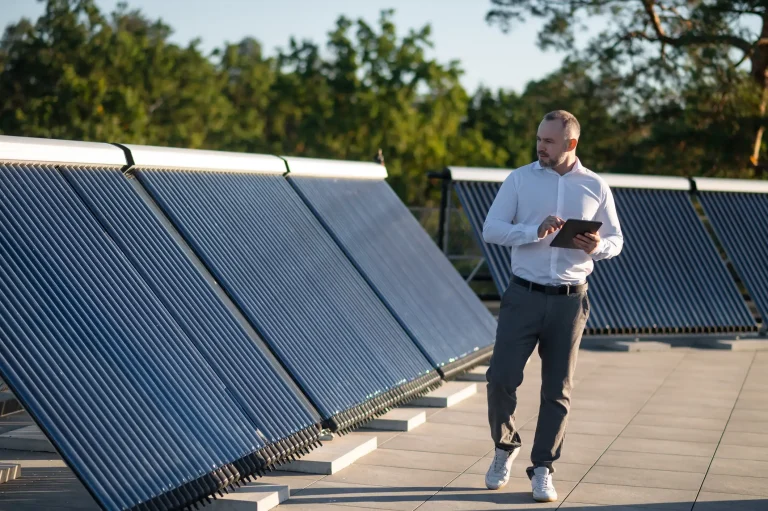 Ein Experte steht auf einem Flachdach neben einer großen Solarthermie-Anlage mit Vakuumröhrenkollektoren und nutzt ein Tablet zur Analyse der Systemleistung.